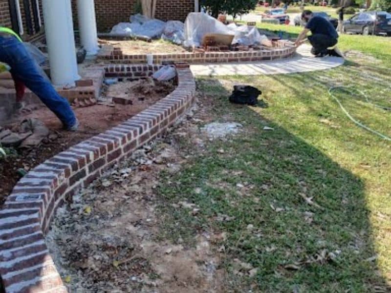 Masonry contractors building a brick garden wall along a front yard walkway