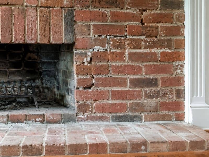 A traditional brick fireplace with visible mortar cracks and light masonry wear inside a cozy living room