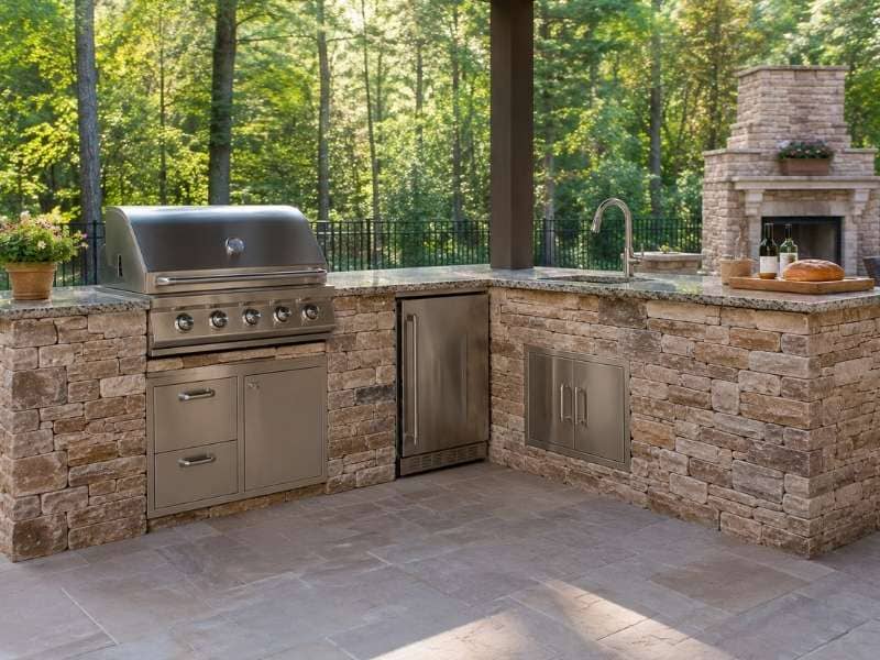 Custom stone outdoor kitchen with a built-in grill and countertop in a backyard patio setting