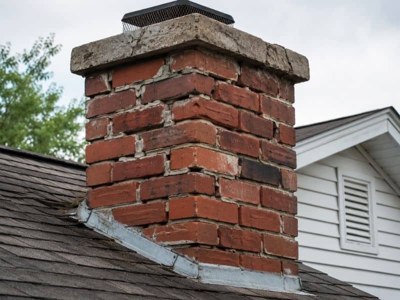Damaged brick chimney with cracked mortar and visible wear on a residential roof showing early signs of chimney masonry repair