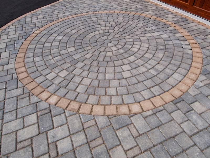 Circular brick paver pattern with contrasting borders creating a timeless look for a driveway or patio.