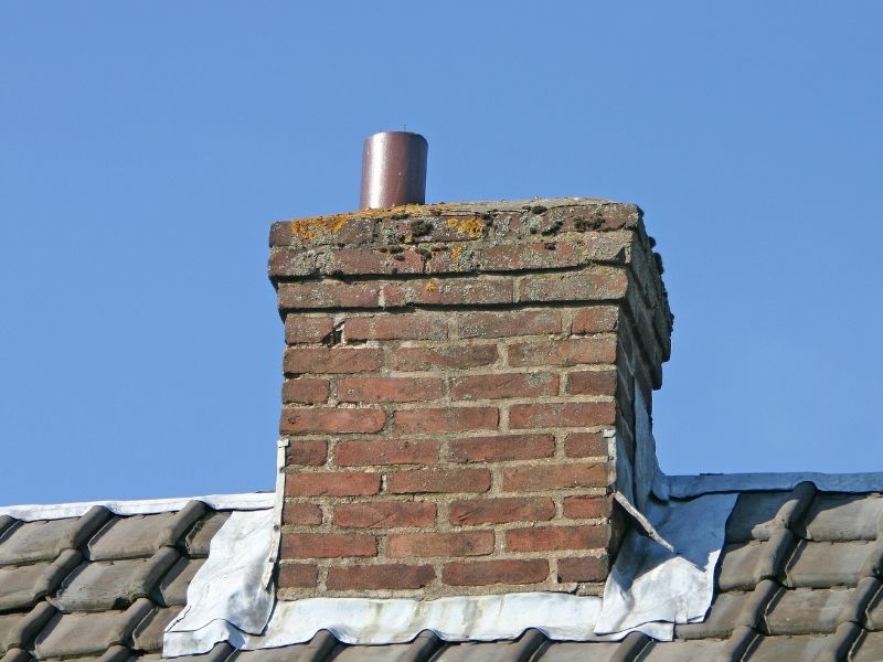 Brick repair concern at metal roof flashing on a weathered exterior brick chimney in Huntsville, Alabama.