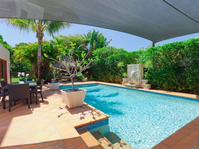 Backyard swimming pool with terracotta tile patio, outdoor dining area, and lush greenery
