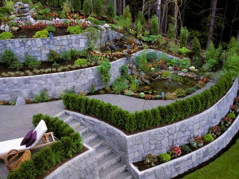 Terraced stone garden with a small pond, manicured hedges, and a seating area on the steps.